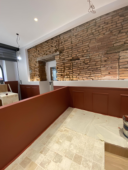 Travaux de peinture en cours dans un local en briques typiques de la région toulousaine, avec application d’une finition rouge satinée sur boiseries murales et murs bas, illustrant un savoir-faire artisanal en Haute-Garonne (31).